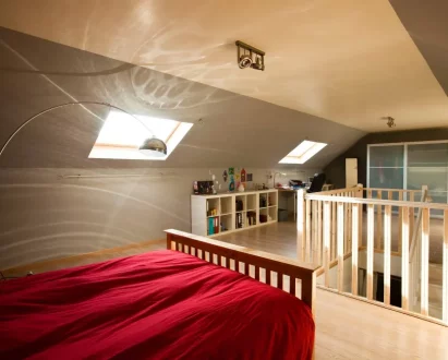 Chambre aménagée sous combles avec lit en bois, mezzanine et rangements intégrés sous toiture